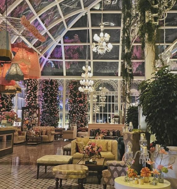 An indoor event setting with flowers, pendant lamps and chandeliers